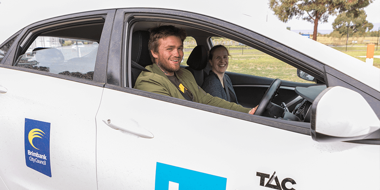 A young man and woman sit in a vehicle with the L2P and Brimbank Council logo on the side of the car.