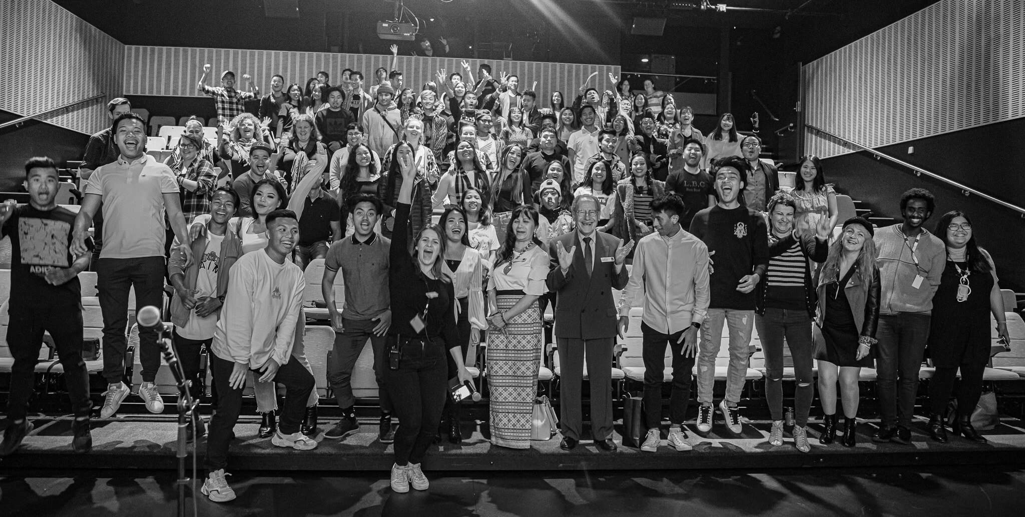 A big group of people on the steps of a cinema smile and cheer at the camera