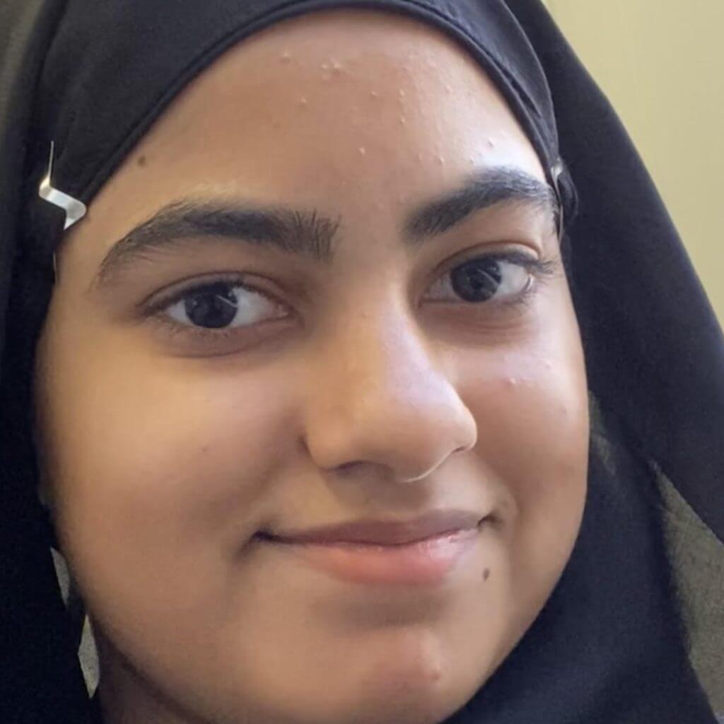 A selfie of Asna wearing a black head scarf and smiling at the camera