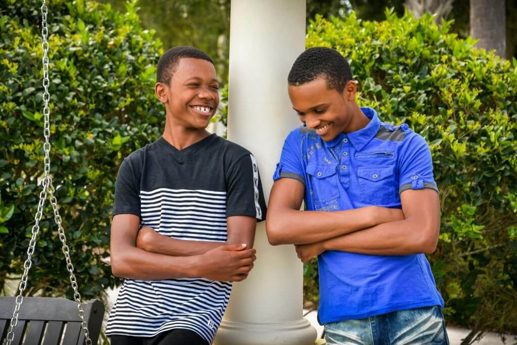 Two boys lean against a pole with their arms crossed are smiling