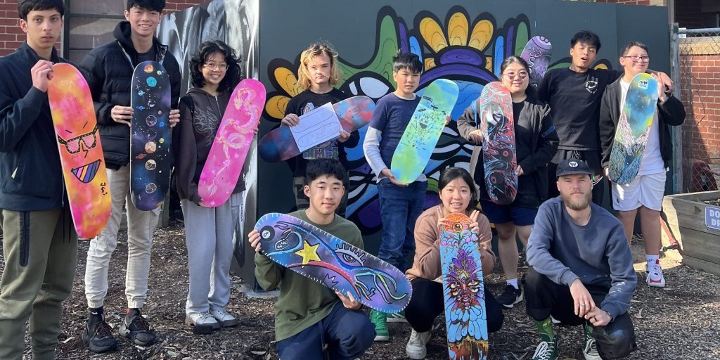 A group of young people holding up vibrantly decorated skateboard decks.