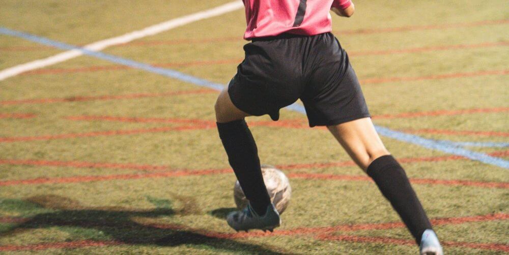 a female soccer player kicks a ball across a field