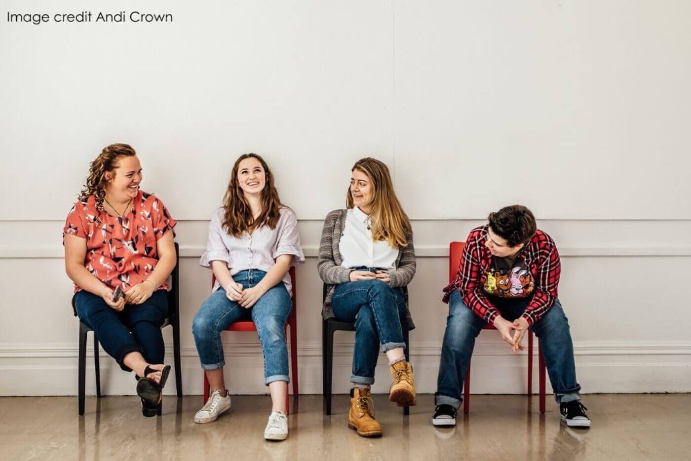 Four women sit on chairs while smiling and laughing