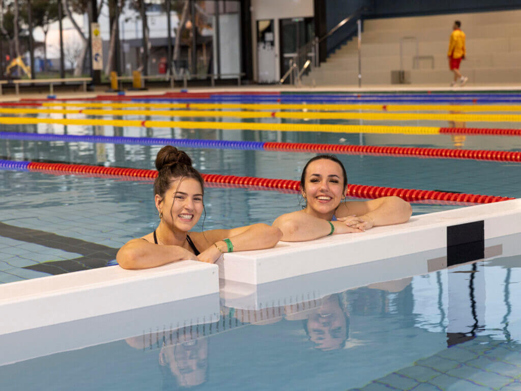 Two women are in a swimming pool and smiling
