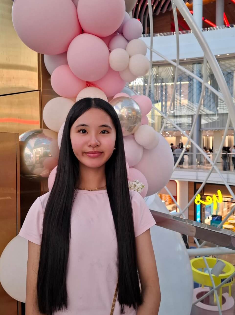 Jayda is wearing a pink shirt and smiling at the camera. Behind her there is a pink and silver balloon sculpture.