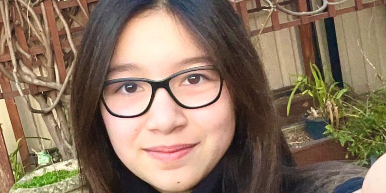 Cara Ramsay takes a selfie and smiles at the camera. She is wearing black glasses