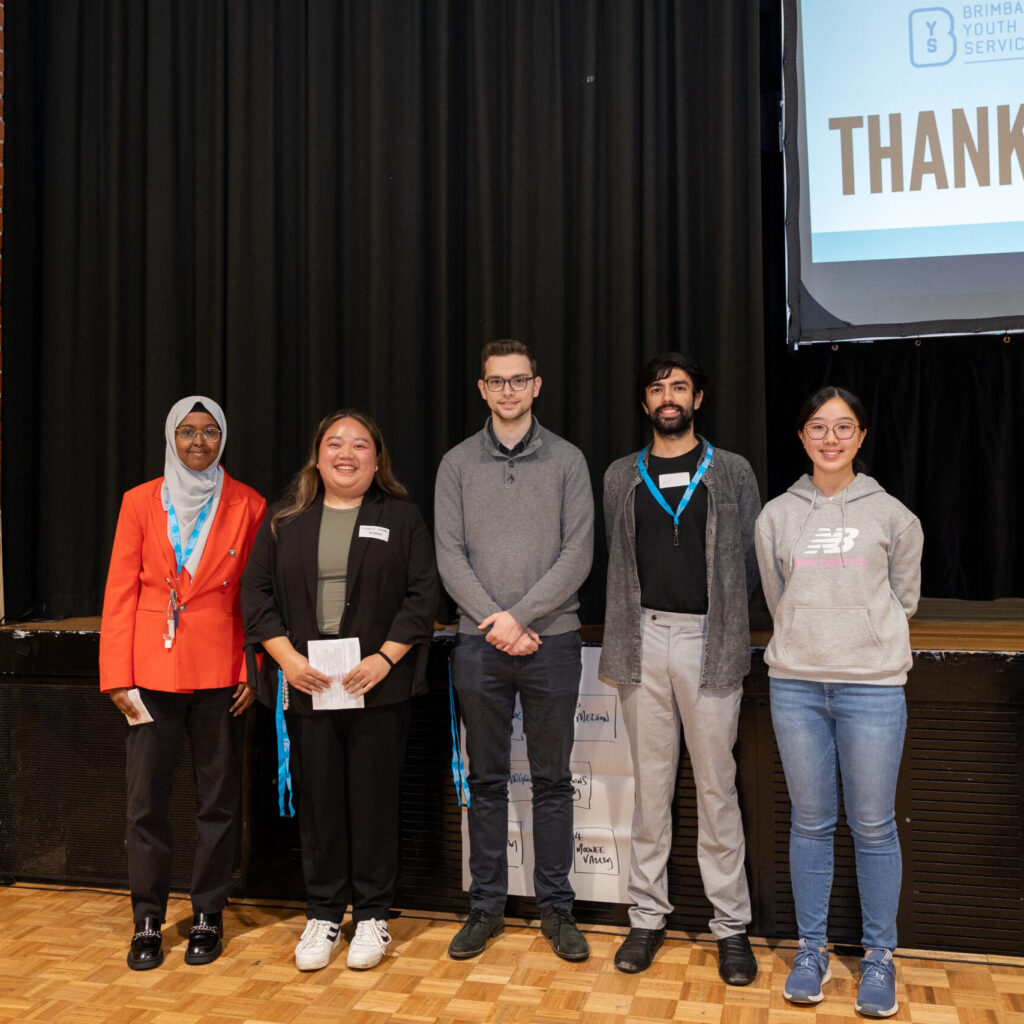 A group of young people are standing in front of a stage smiling at the camera