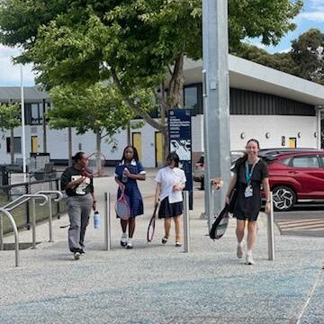 A group of young girls and an older facilitator carry sports equipment down the street.