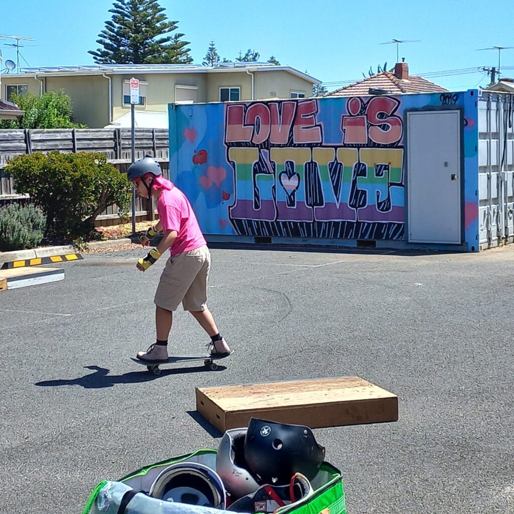 One person wears a helmet and skateboards, with a mural that says "Love is Love" behind them