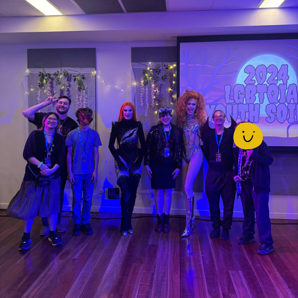 A group of people pose with two drag queens under purple light