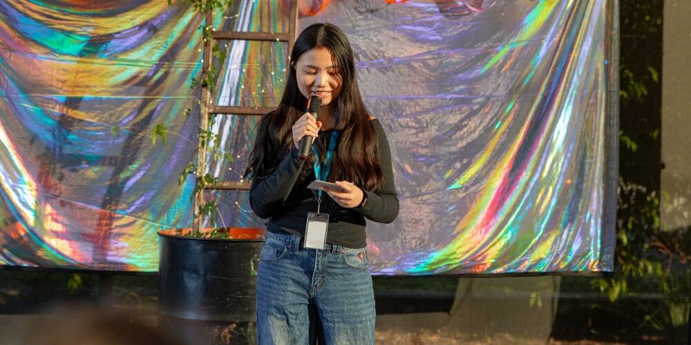 A girl speaks into a microphone while standing in front of a holographic backdrop