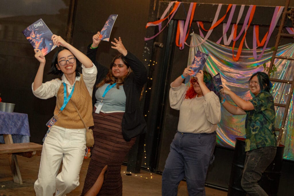A group of young people dance while holding up The Bold Source magazine